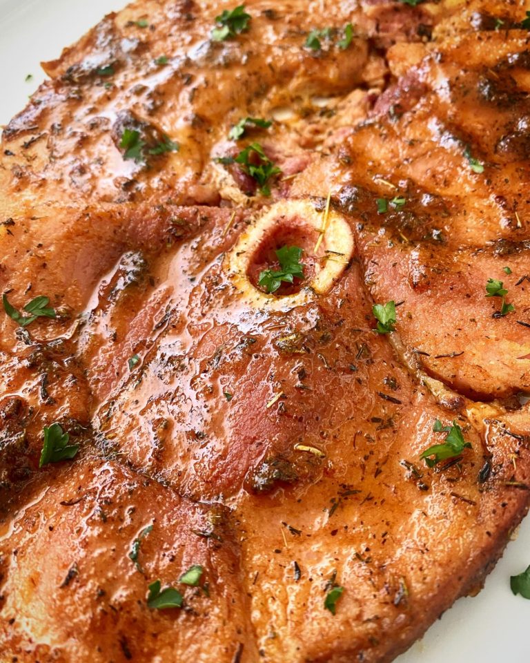 close up show of shot of cooked ham steak on a white plate garnished with fresh parsley