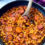 pork and beans in a cast iron skillet with a wooden spoon