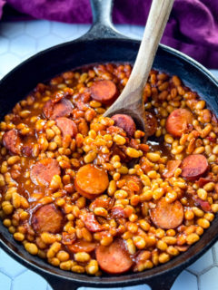 pork and beans in a cast iron skillet with a wooden spoon