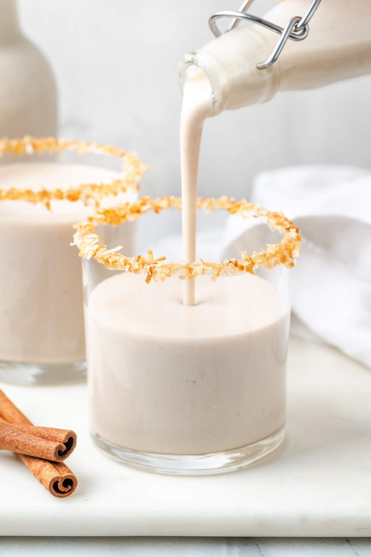 Pouring vegan coquito into glass with toasted coconut rim