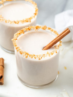 Two glasses of vegan coquito with toasted coconut rims