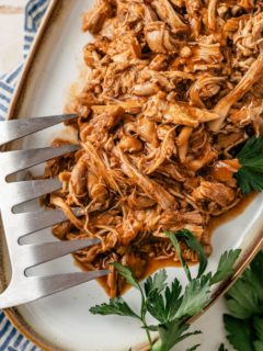 A large plate overflowing with succulent, pulled BBQ chicken, glistening in barbecue sauce, ready to be served.