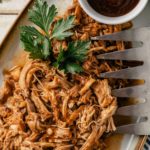 A delicious serving of juicy, pulled BBQ chicken on a large plate, with tender strands glazed in a rich, smoky barbecue sauce.