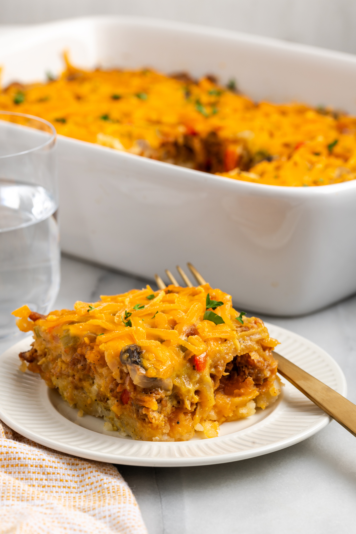 Vegan hashbrown breakfast casserole on plate with fork, with casserole dish in background