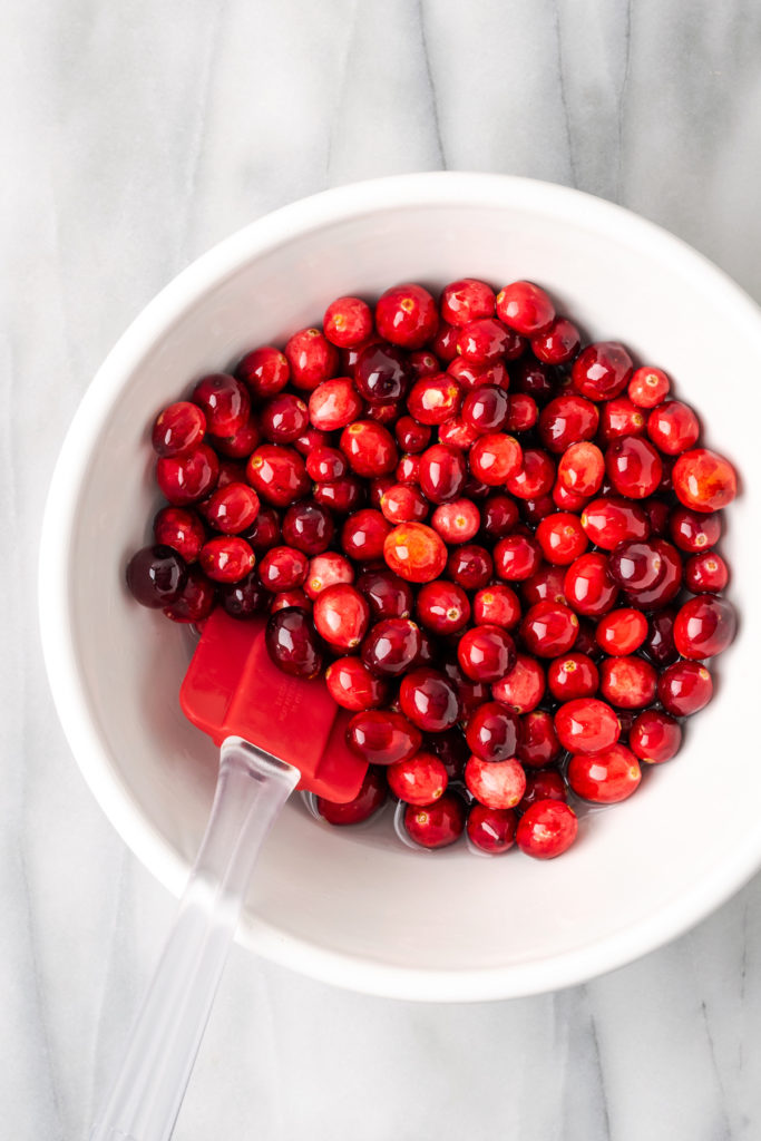 Overhead view of cranberries in bowl with rubber spatula, stirring into simple syrup