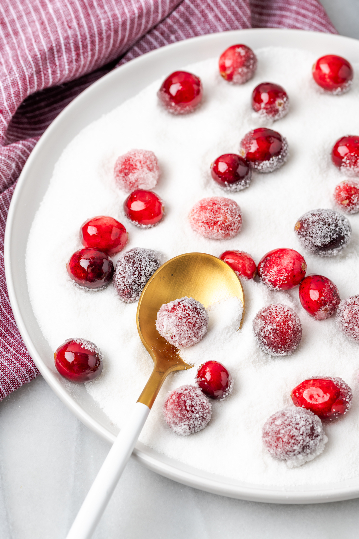 Cranberries being coated in sugar on white plate with spoon