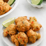 Freshly fried saltfish fritters recipe on a white plate with lime wedges