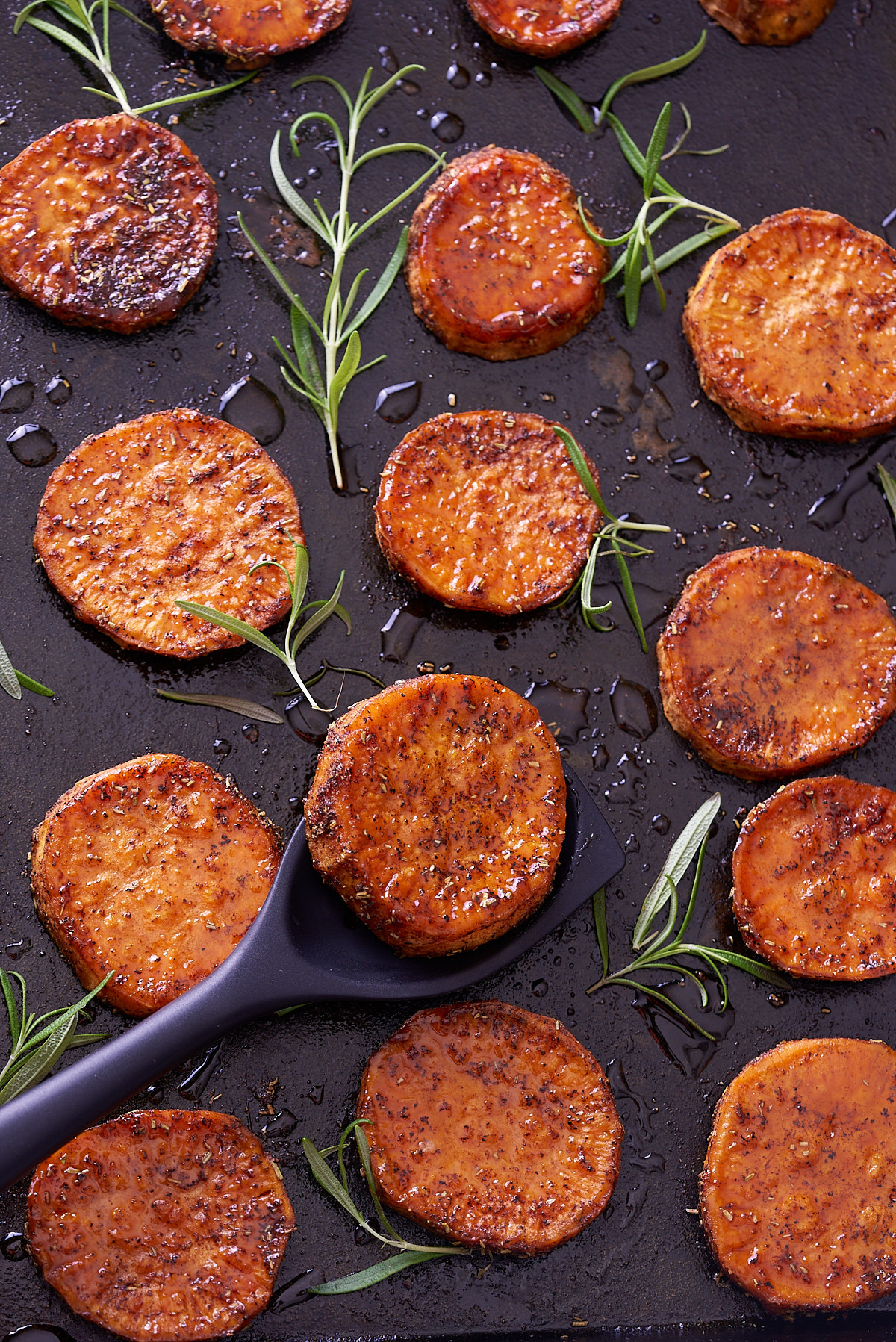 baked sweet potato rounds on baking sheet with spoon picking them up