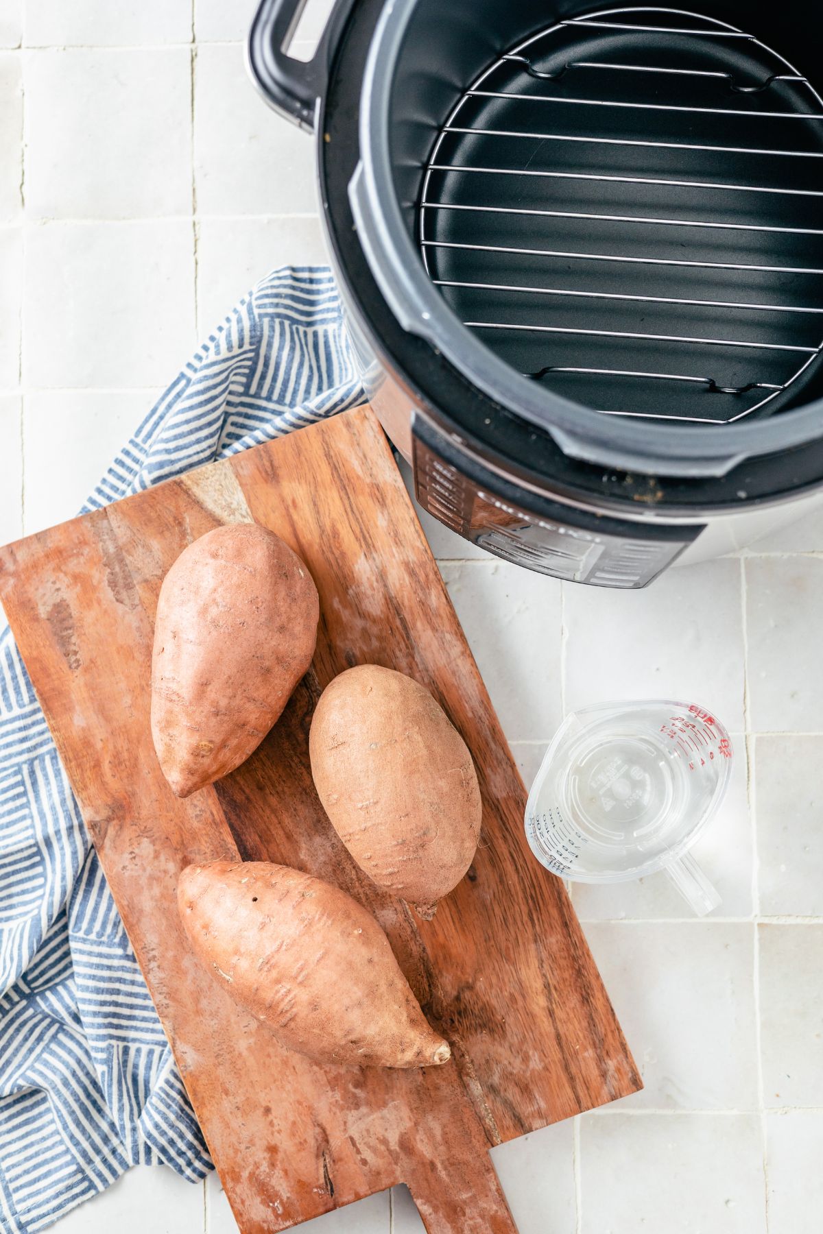 Fresh large sweet potatoes beside a measuring cup filled with one cup of water - Ingredients for making Instant Pot Sweet Potatoes