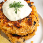 Stack of 2 vegan crab cakes on plate topped with tartar sauce