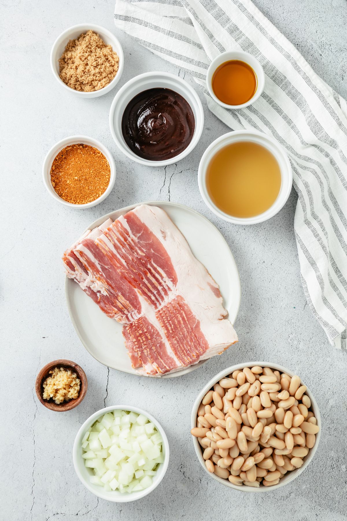 Ingredients for Baked Beans With Canned Beans: No sugar-added bacon, yellow onion, minced garlic, low-sodium chicken broth, cannellini beans, BBQ seasoning, hickory or Kansas City style BBQ sauce, brown sugar, and a touch of Hennessy for a flavorful twist.