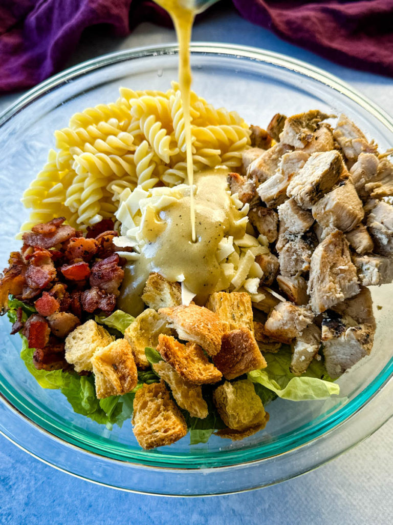 chicken pasta salad with bacon drizzled with salad dressing in a glass bowl