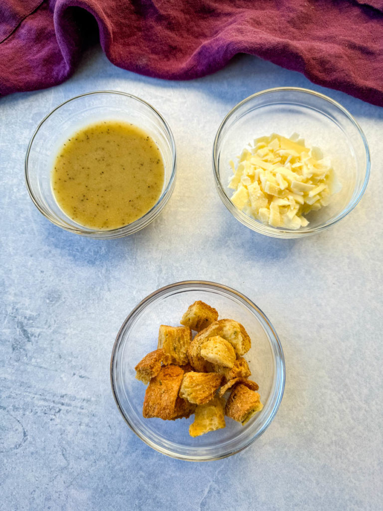 salad dressing, grated cheese, and croutons in separate glass bowls