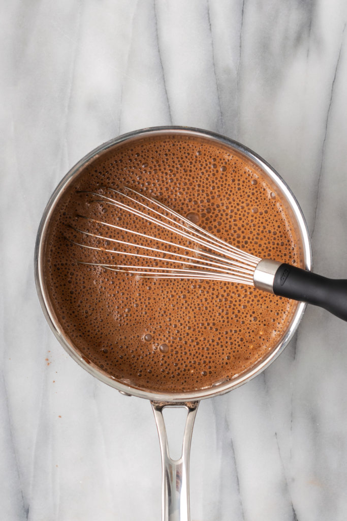Overhead view of chocolate pudding cooking in saucepan with whisk