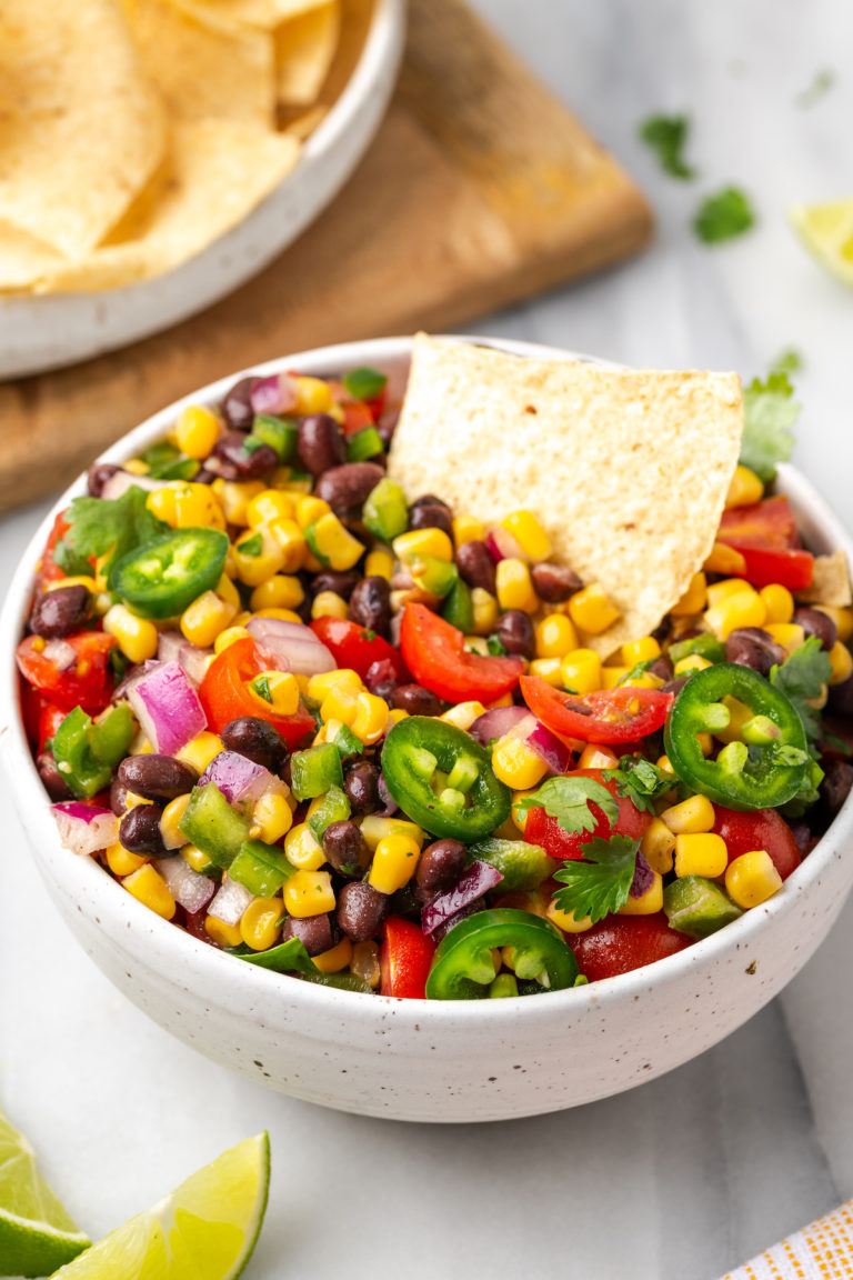 Tortilla chip in bowl of fresh corn salsa