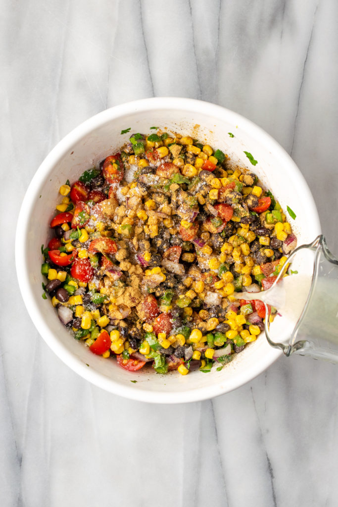 Pouring lime juice into bowl of corn salsa