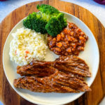 Crockpot brisket on a plate with coleslaw, baked beans, and broccoli