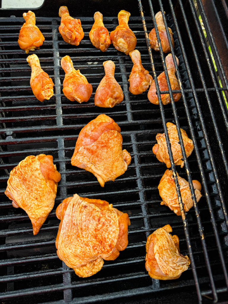 raw seasoned chicken drumsticks and chicken thighs on a grill