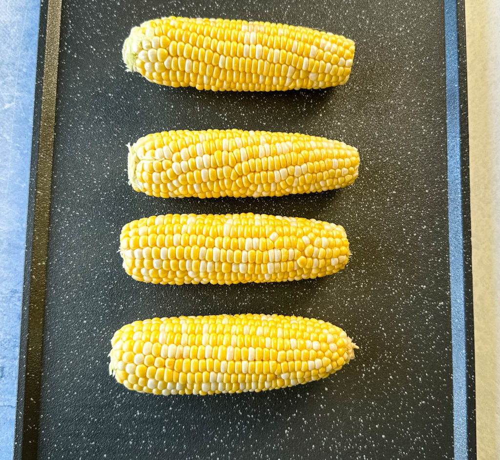 fresh corn on the cob on a sheet pan