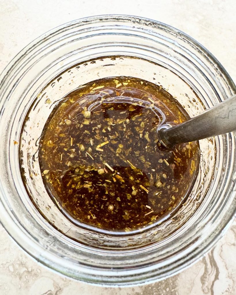overhead shot of grilled vegetable marinade in a glass mason jar with a silver spoon