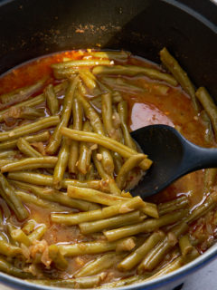 smothered green beans in pot with spoon stirring the beans
