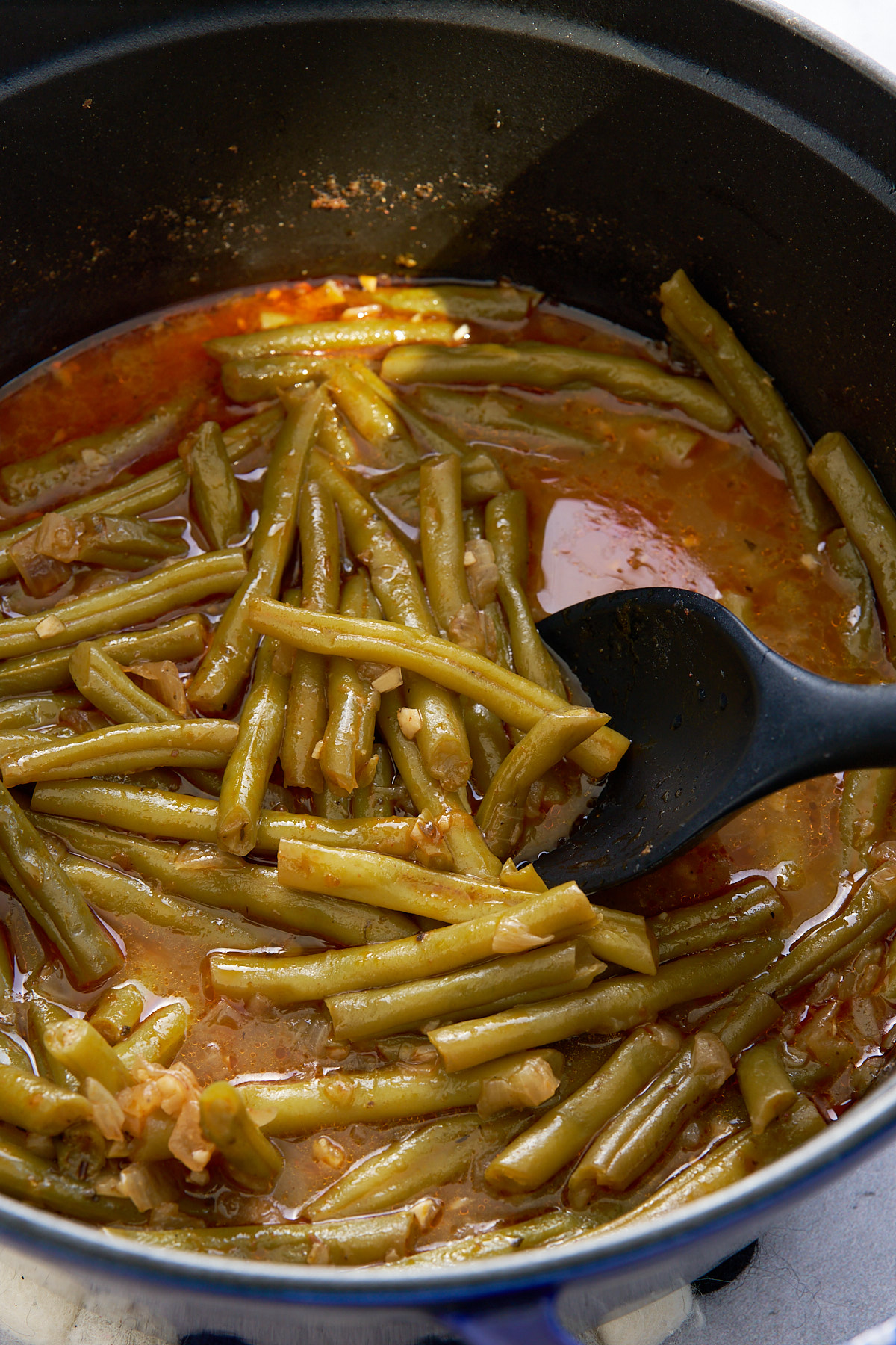 smothered green beans in pot with spoon stirring the beans