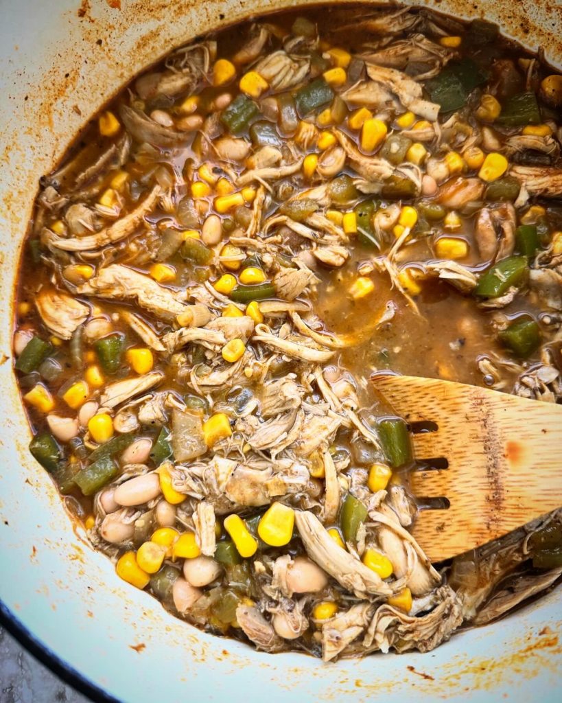overhead shot of white chicken chili white dutch oven with a wooden spoon
