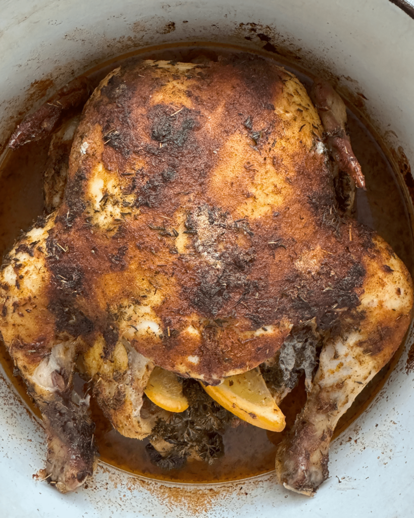 overhead shot of cooked, roasted chicken in a white Dutch oven
