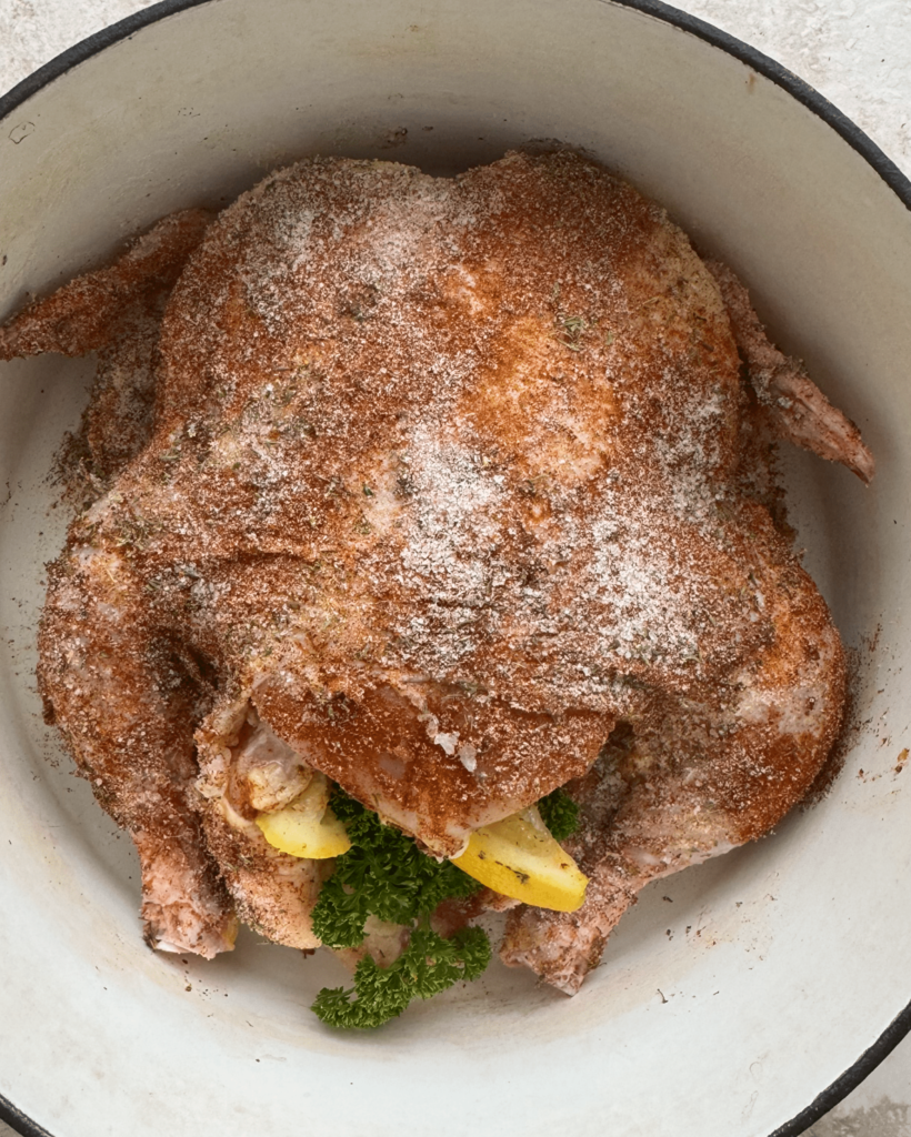overhead shot of unooked, roasted chicken in a white Dutch oven