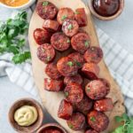 Air fryer smoked sausages on a wooden board with ketchup and mayo dips on the side