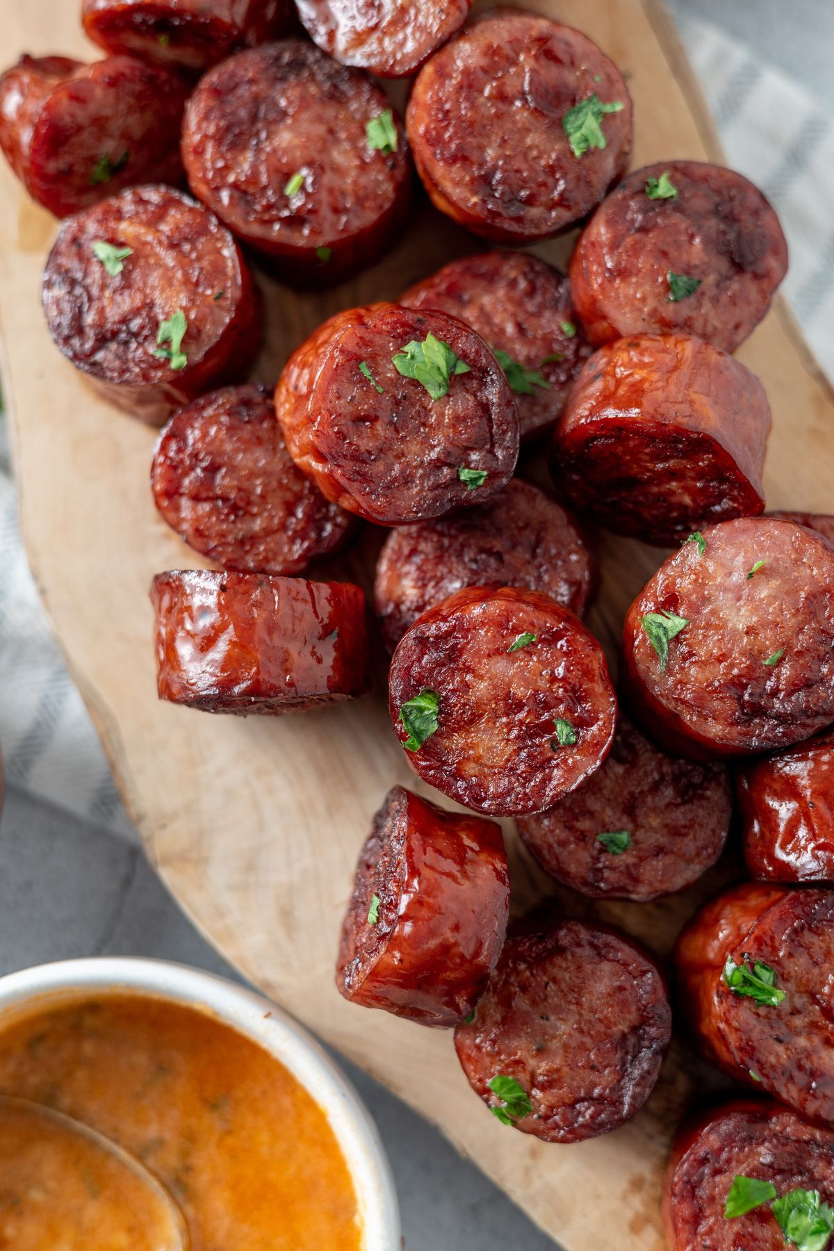 Smoked sausages cooked in an air fryer, served on a wooden board with ketchup and mayo dips on the side