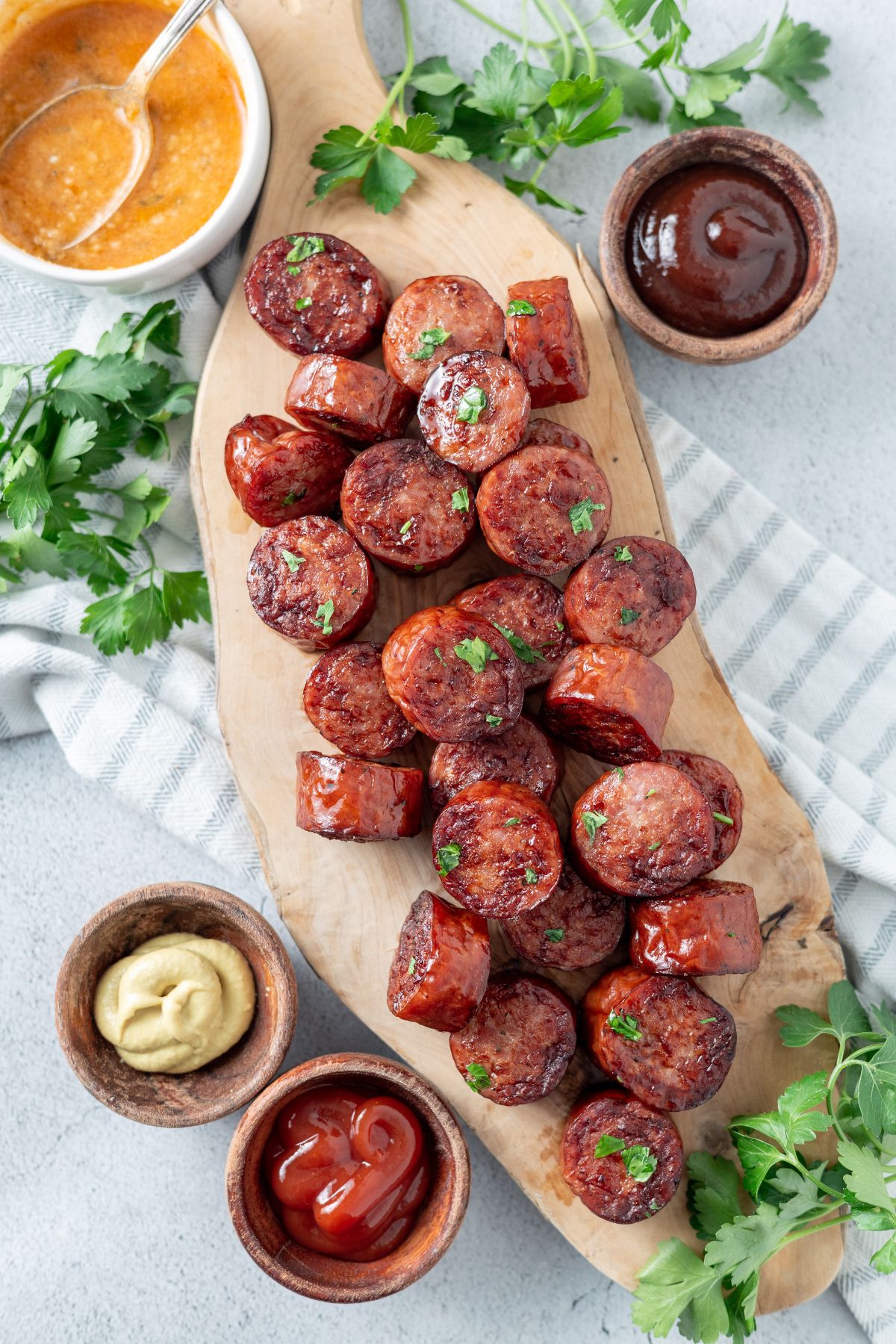 Air fryer smoked sausages on a wooden board with ketchup and mayo dips on the side