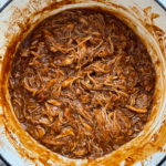 overhead shot of shredded bbq pulled chicken in a white dutch oven