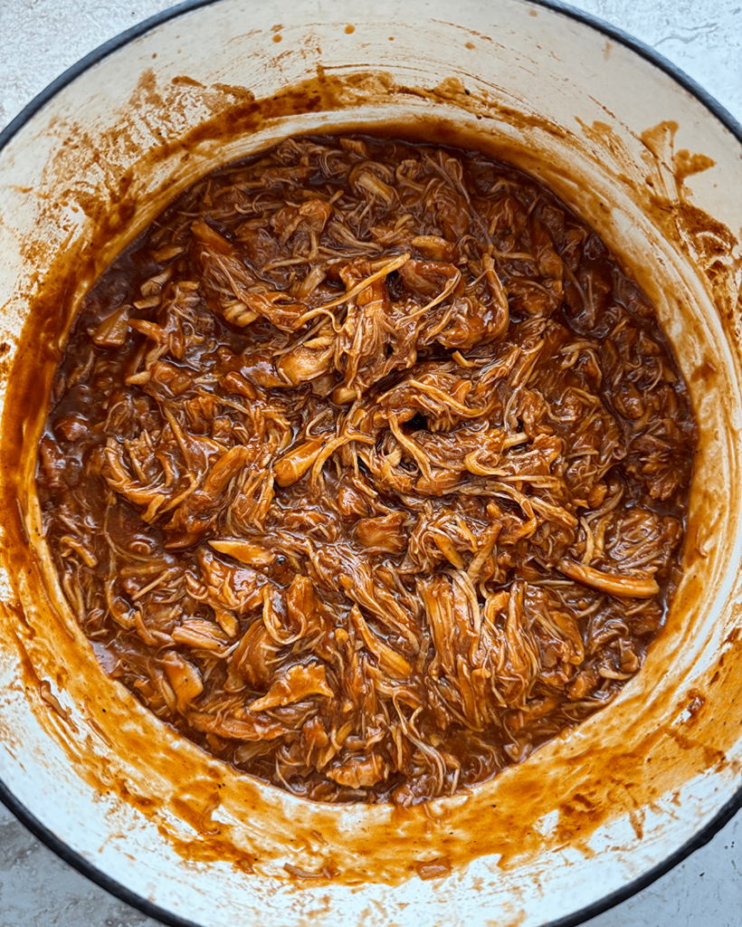 overhead shot of shredded bbq pulled chicken in a white dutch oven
