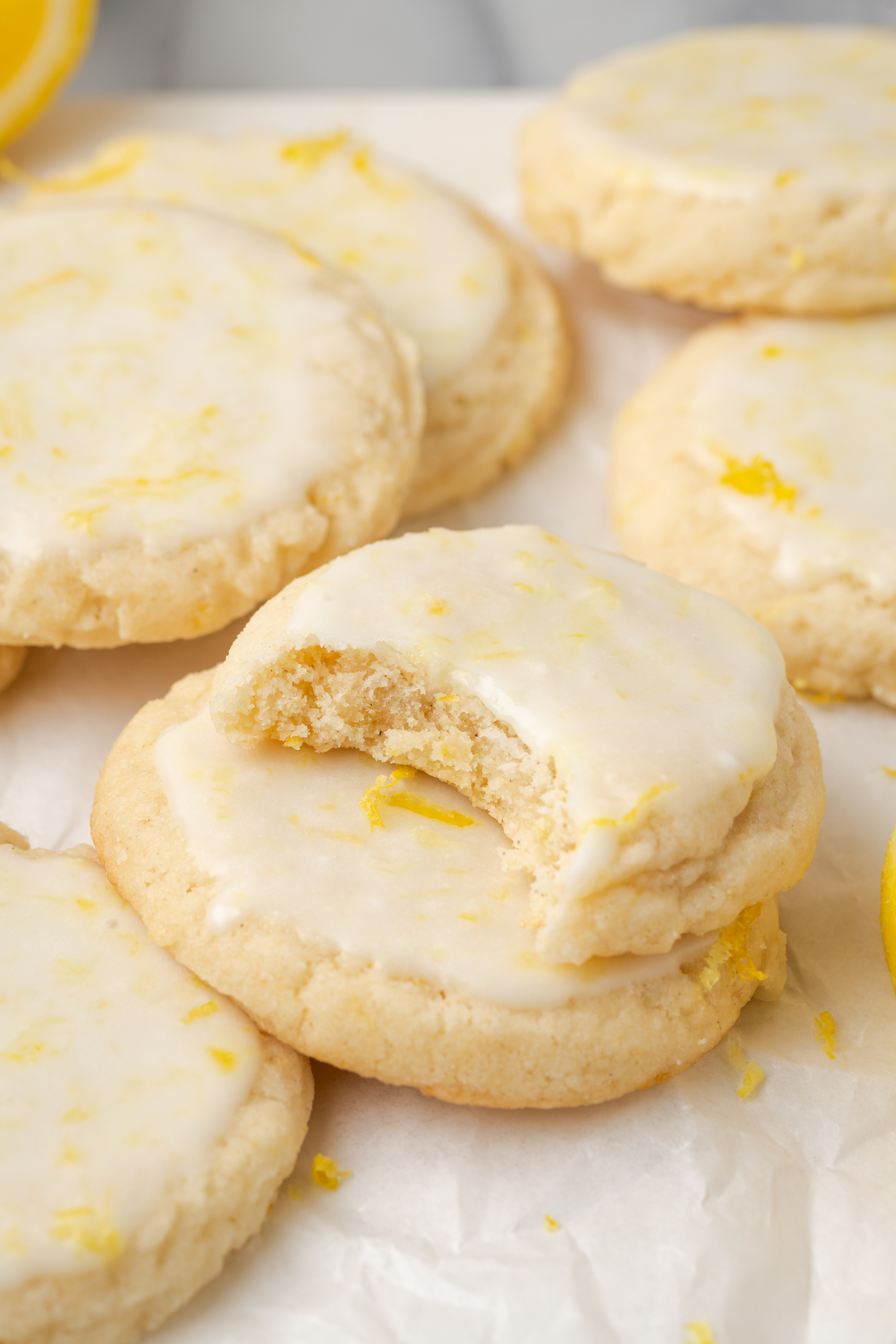 Lemon cookies on crumpled parchment paper, with bite taken out of one to show soft texture