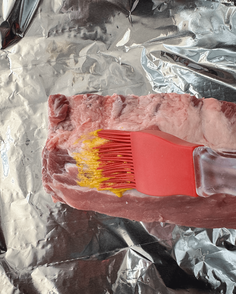 overhead shot of uncooked, ribs on a sheet of foil with mustard being spread on top