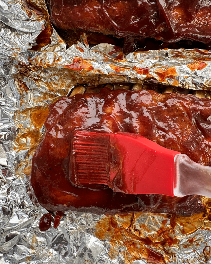 overhead shot of cooked, baked ribs with BBQ sauce on a sheet of foil