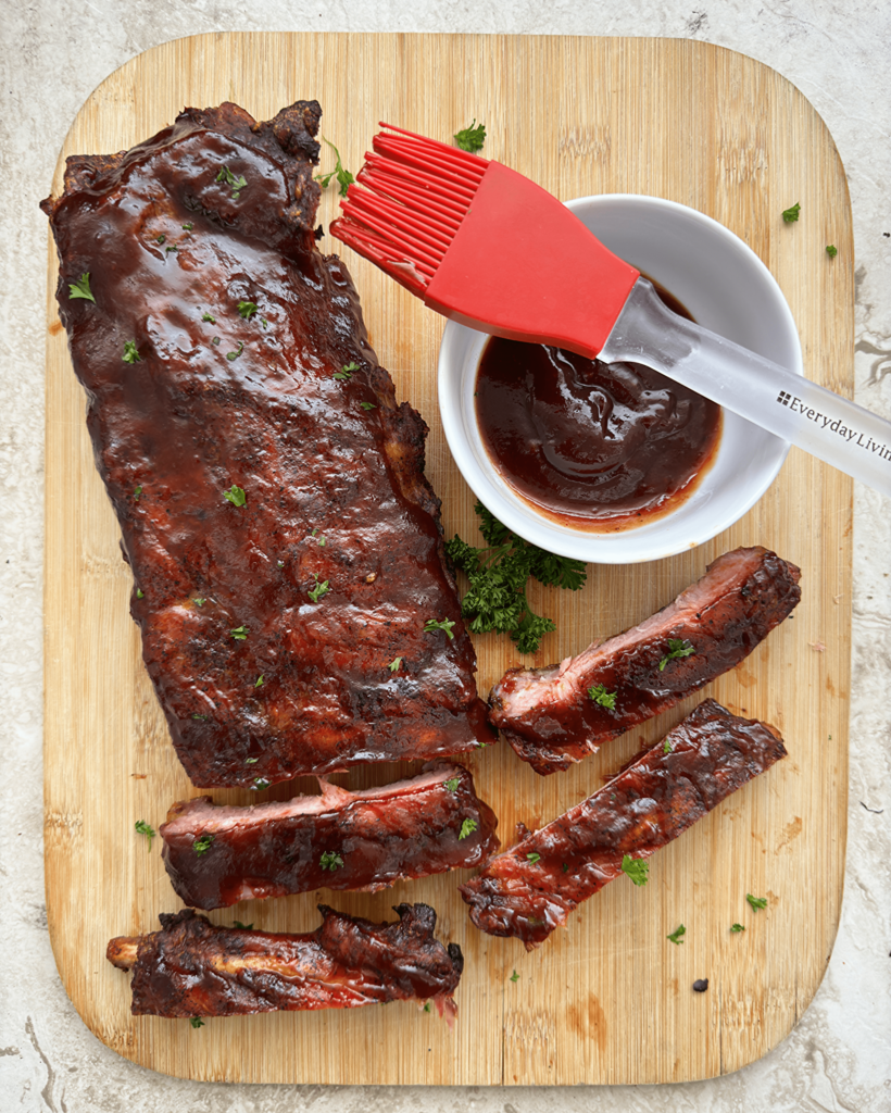 overhead shot of bbq baby back ribs on a wooden cutting board with a bowl of BBQ