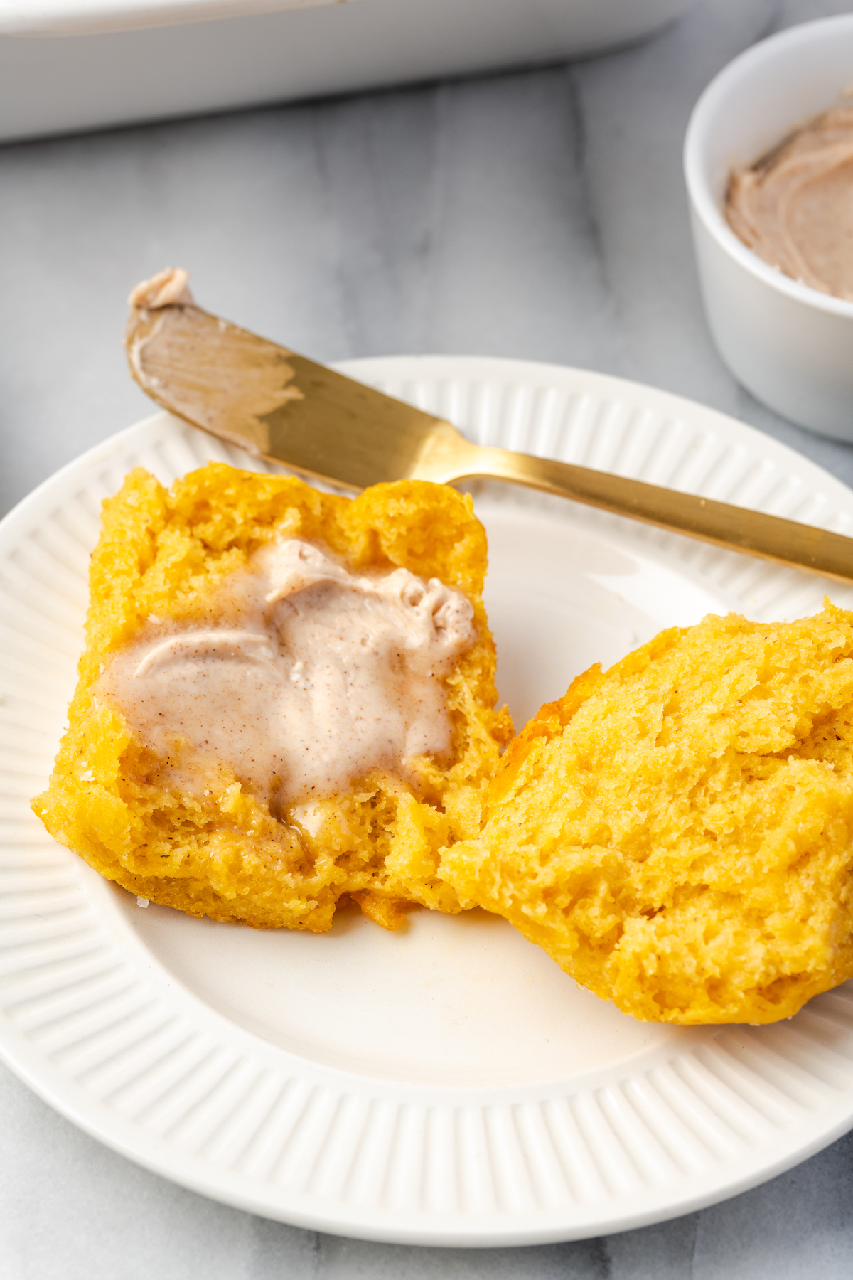 Sweet potato roll cut in half on plate with cinnamon butter spread on top