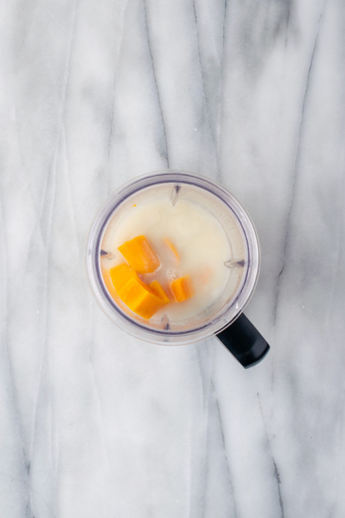 Overhead view of sweet potatoes added to water and soy milk in blender