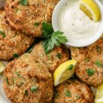 Golden-brown salmon patties with a creamy mayo dip on a plate.