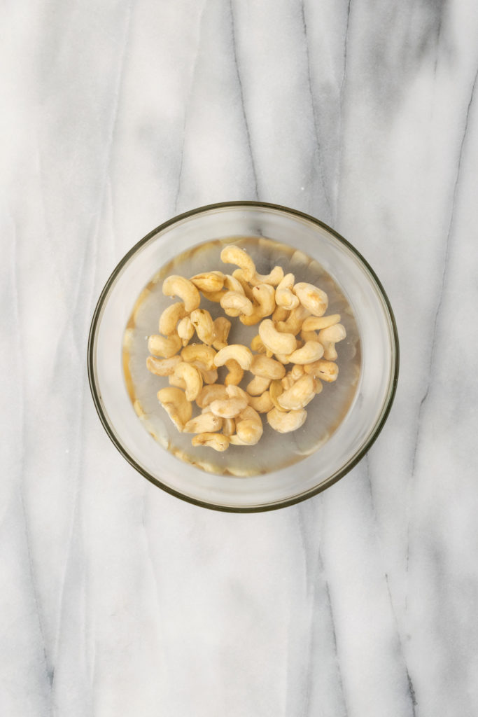 Overhead view of raw cashews in bowl of water