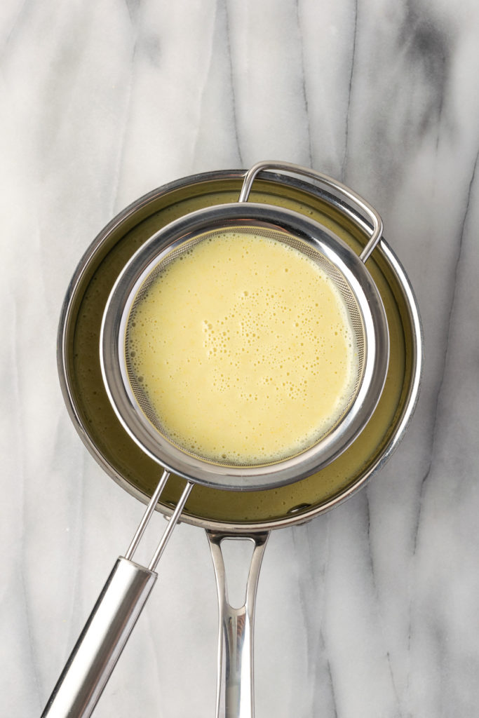 Overhead view of vegan lemon bar filling being poured through strainer