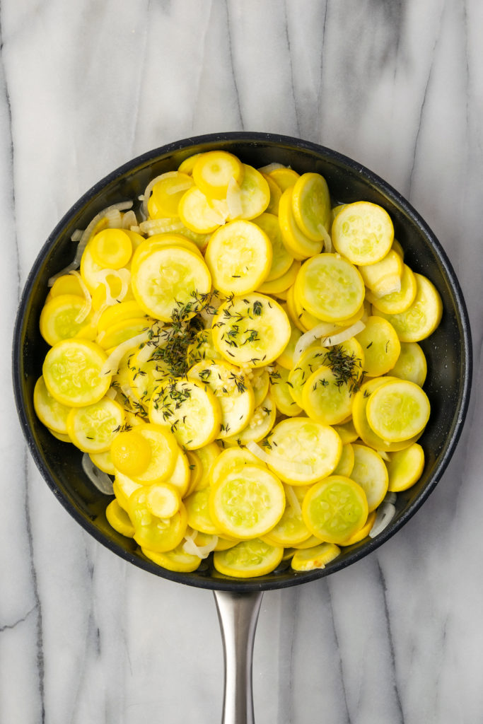 Overhead view of squash, onions, and thyme in skillet